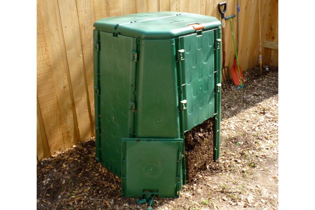 Green compost bin outdoors against a wooden fence