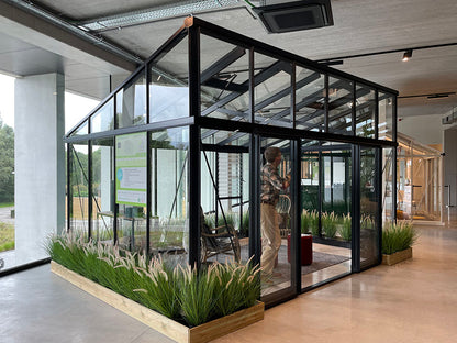 Modern indoor space with glass walls, plants, and a person walking through.