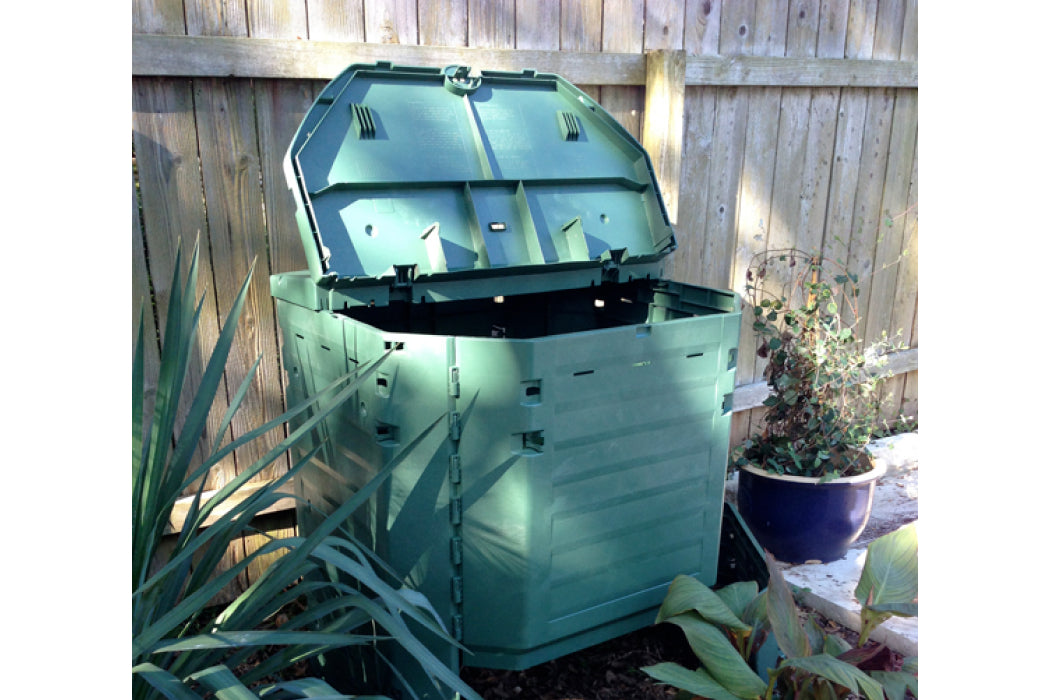 Large Exaco garden compost bin with plants and a wooden fence.