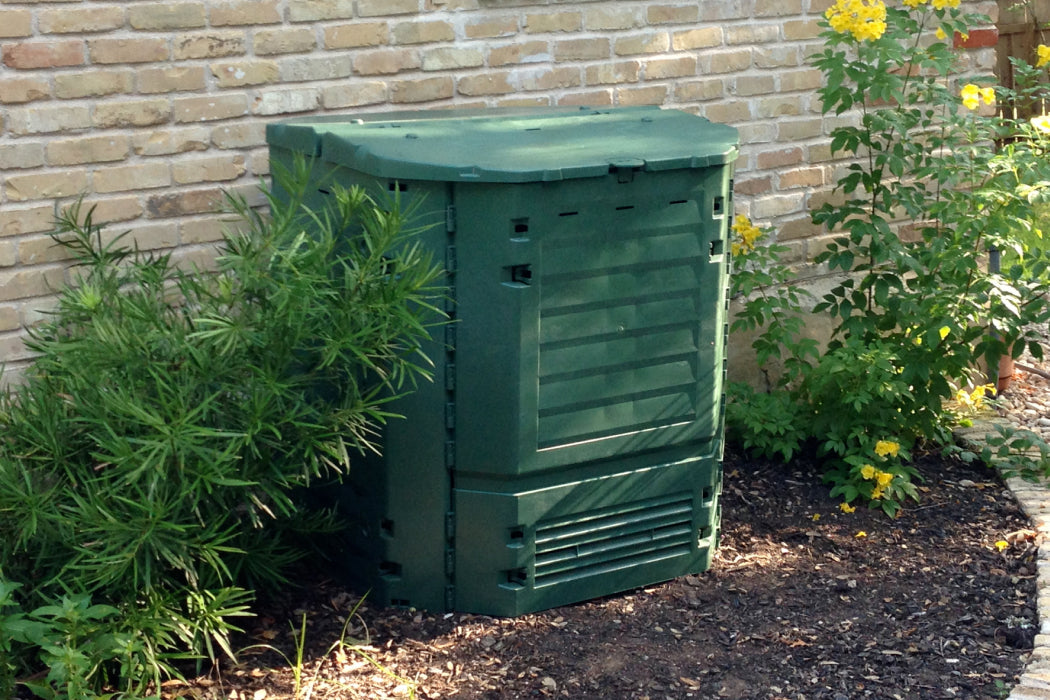 Exaco thermoking compost bin against a brick wall with plants around